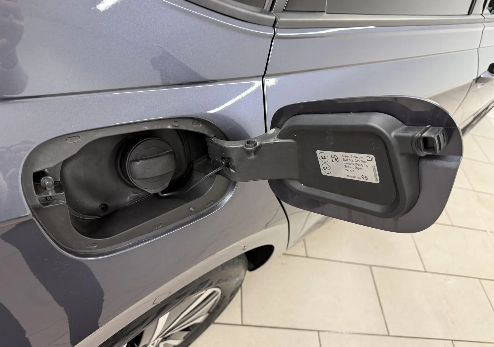 Gros plan sur la trappe à carburant ouverte côté gauche d'une Volkswagen Polo gris cendre avec bouchon essence visible.