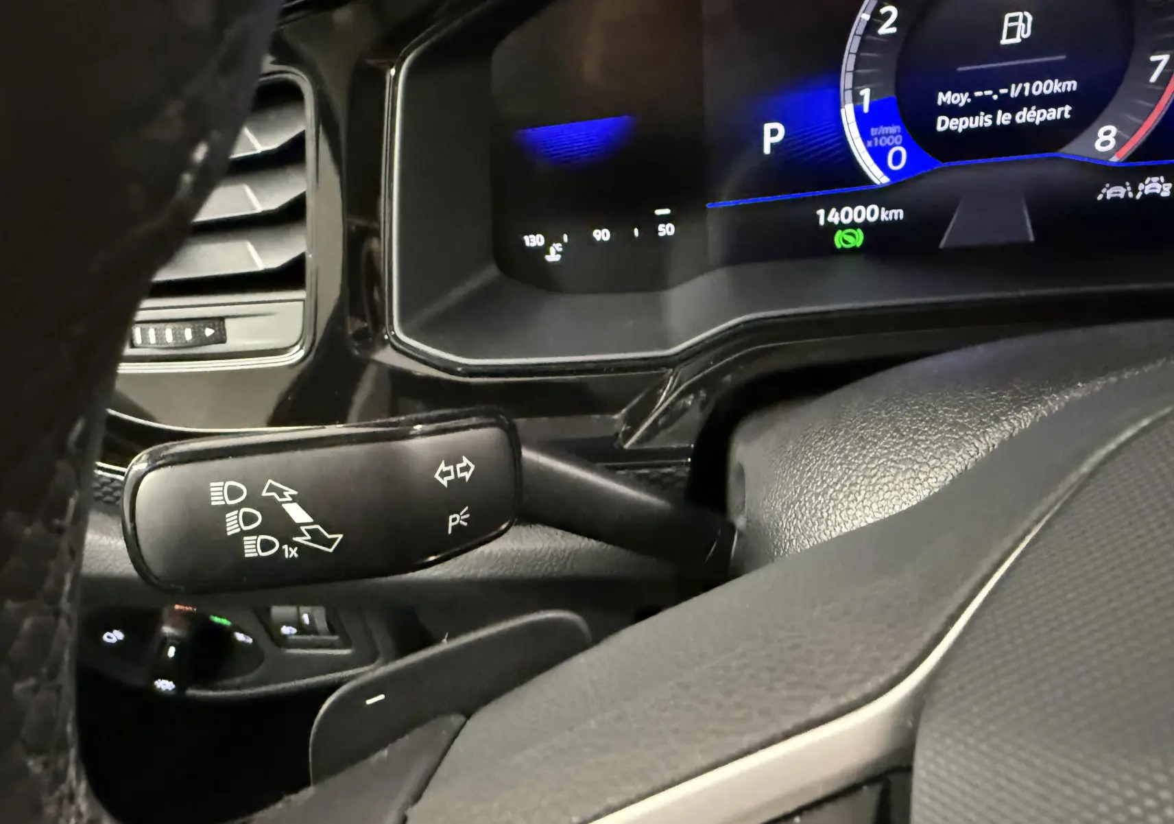 Gros plan sur la manette de clignotants noire et le tableau de bord digital bleu et noir d'une Volkswagen Polo gris cendre.