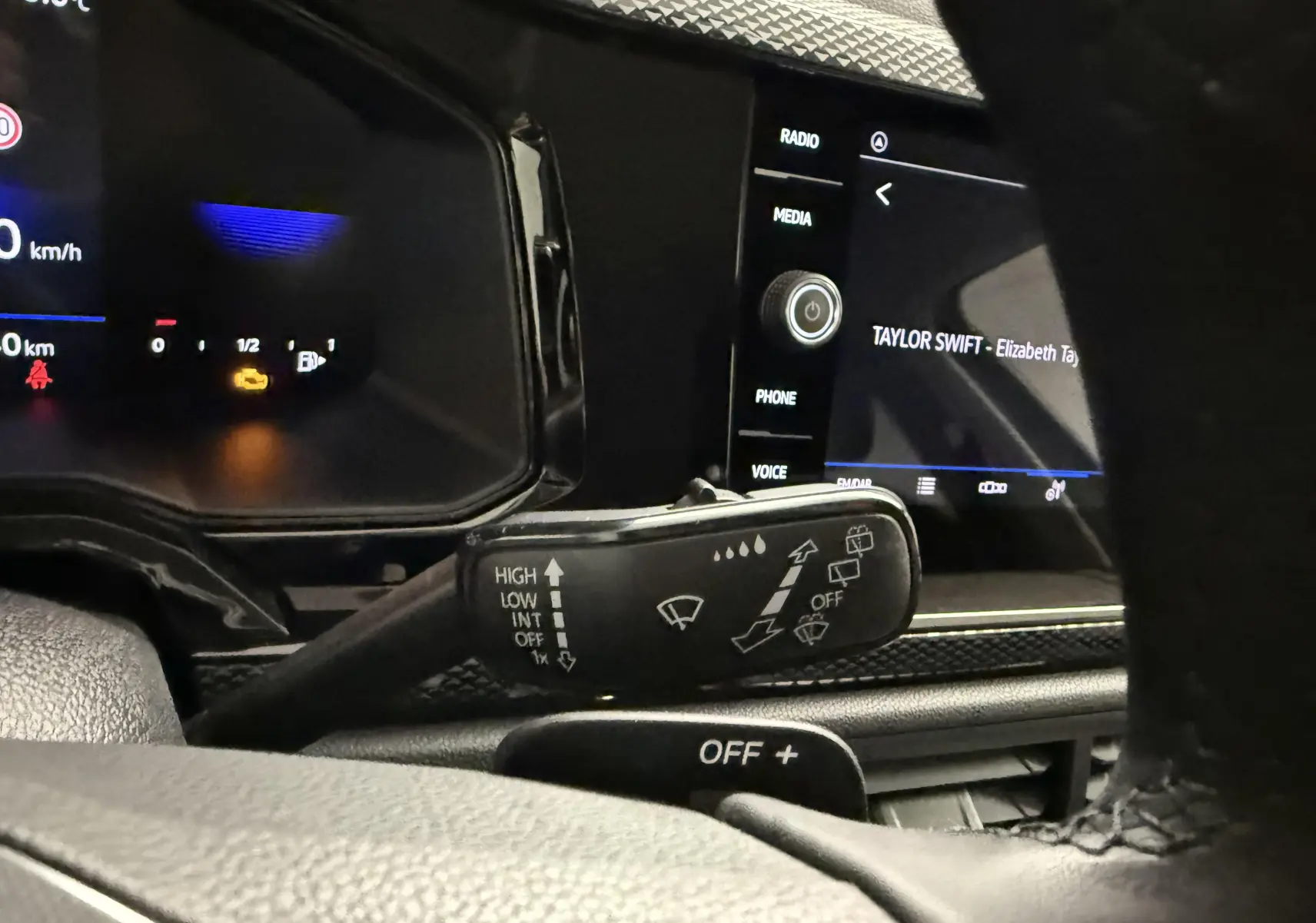 Gros plan intérieur sur la commande d’essuie-glace à gauche du volant d’une Volkswagen Polo gris cendre, avec écran tactile en arrière-plan.