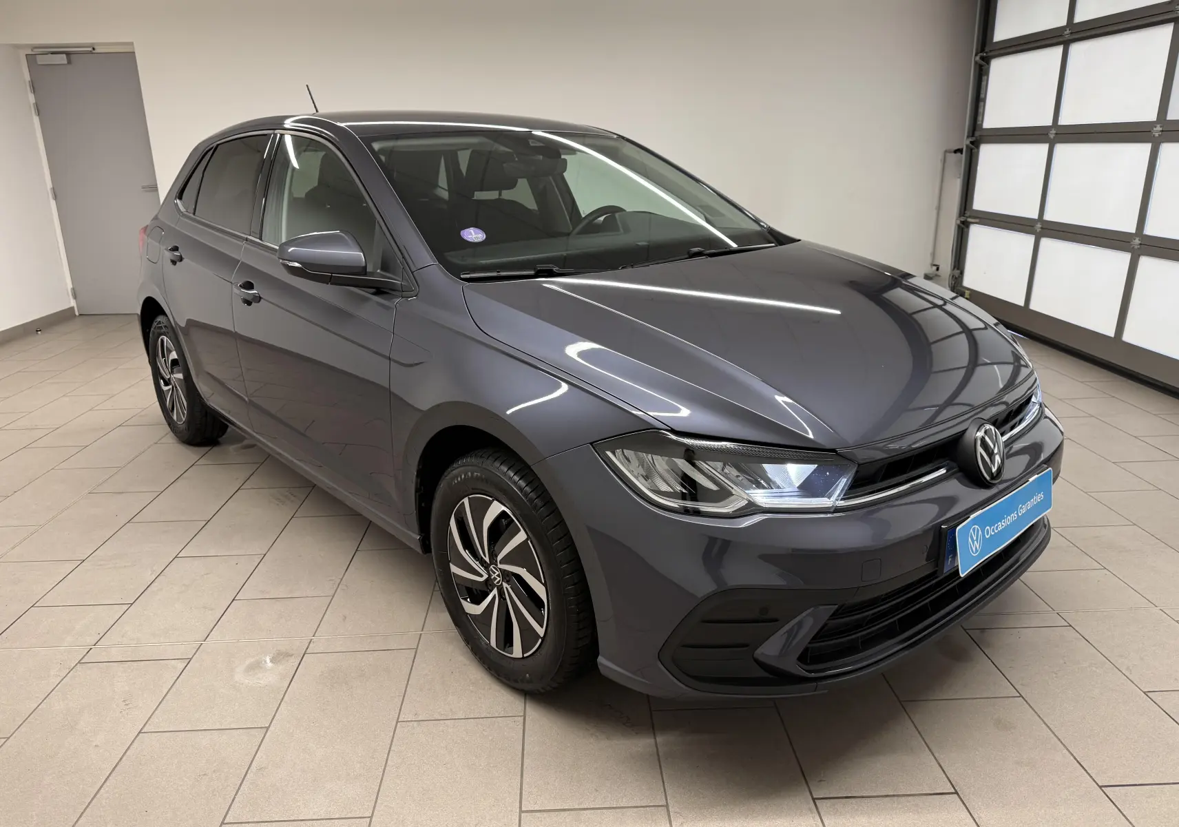 Volkswagen Polo gris cendre vue 3/4 avant droit en intérieur avec jantes alliage et feux LED allumés.