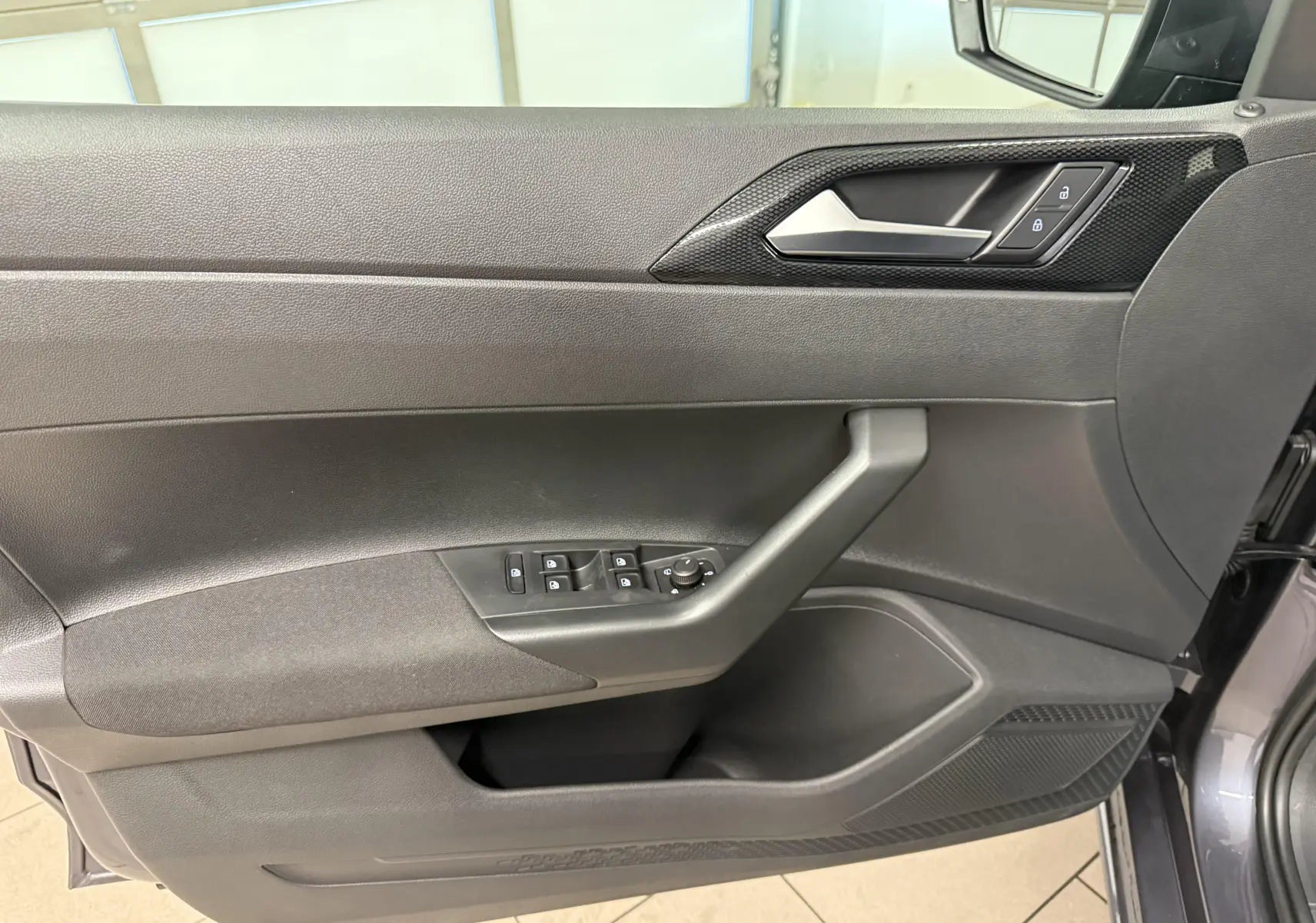 Vue rapprochée de la porte avant gauche de la Volkswagen Polo gris cendre, avec commandes électriques et poignée intégrée.