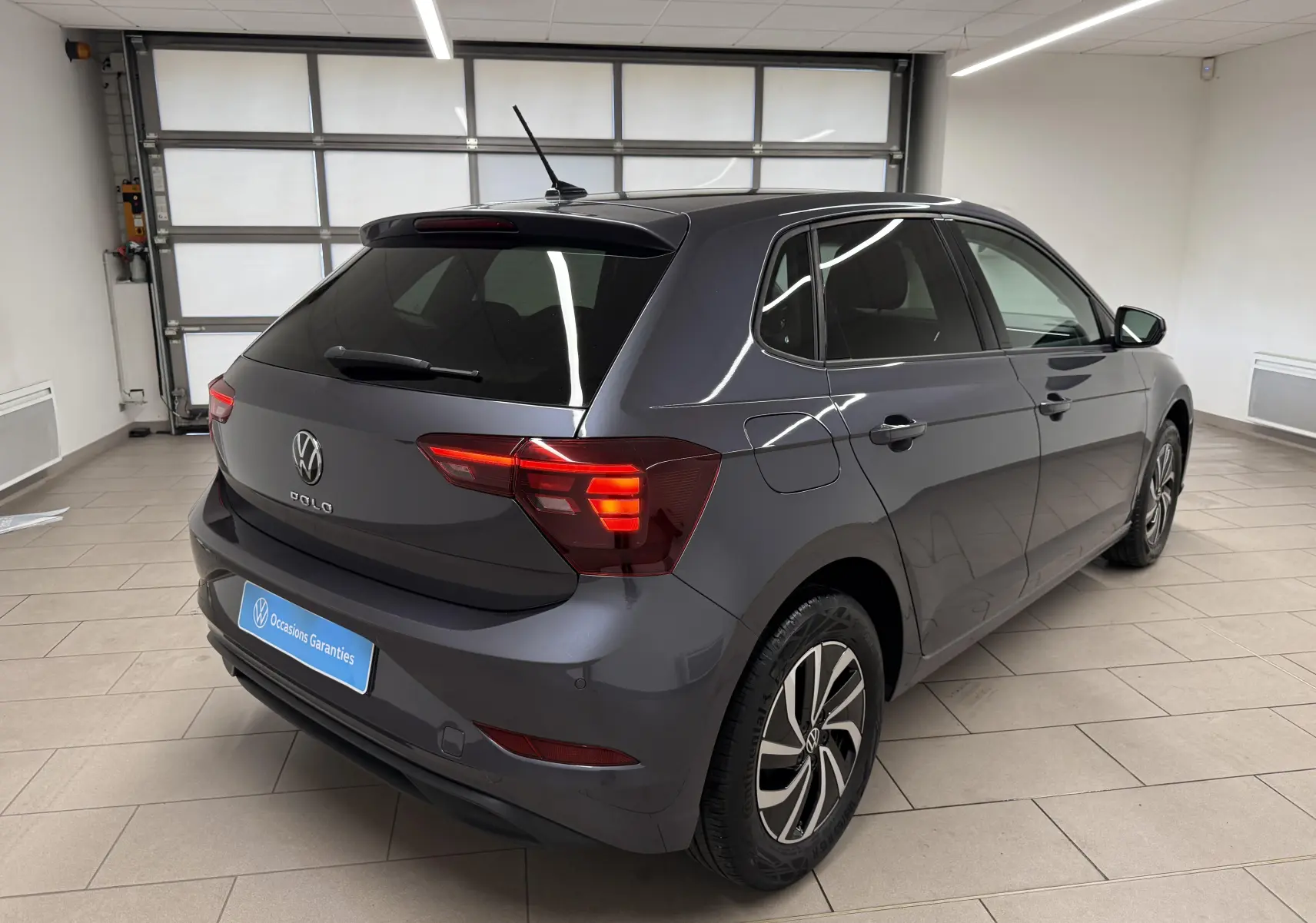 Vue 3/4 arrière droite d'une Volkswagen Polo gris cendre avec jantes alliage et vitres teintées en intérieur showroom.