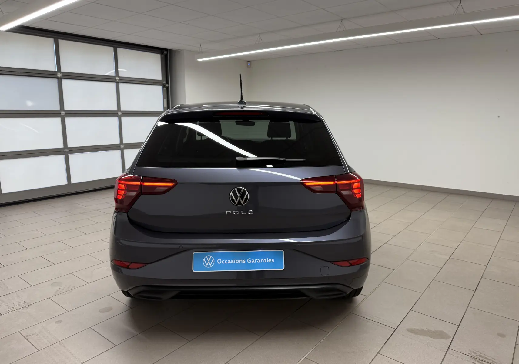 Vue arrière d'une Volkswagen Polo gris cendre 2025 avec feux arrière LED dans un garage lumineux.