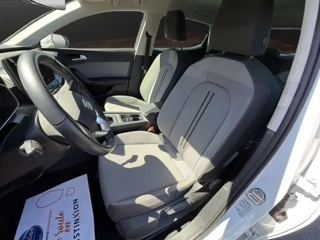 Intérieur de la SEAT LEON blanc vue côté conducteur, montrant sièges tissu gris et volant cuir multifonctions.