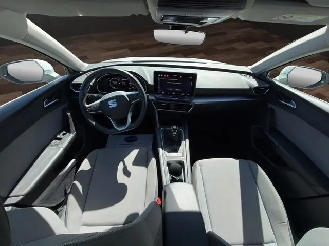 Vue intérieure frontale du poste de conduite du SEAT Leon blanc, avec volant cuir multifonctions et écran tactile central.