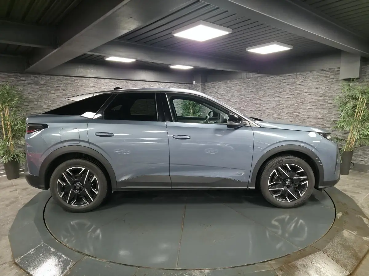 Profil droit d’un Peugeot 3008 hybride 2025 bleu métallisé avec jantes alliage noires et toit noir dans un showroom.