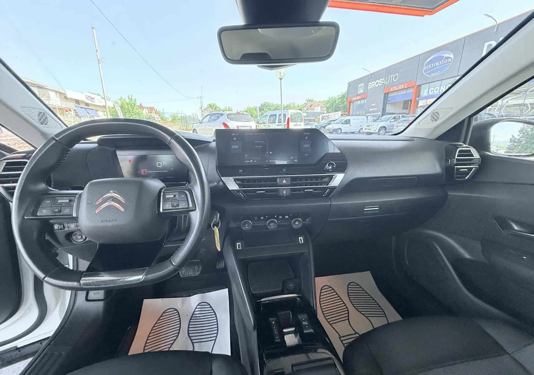 Vue intérieure avant de la Citroën C4 blanche 2023, tableau de bord noir avec écran tactile et volant multifonction.