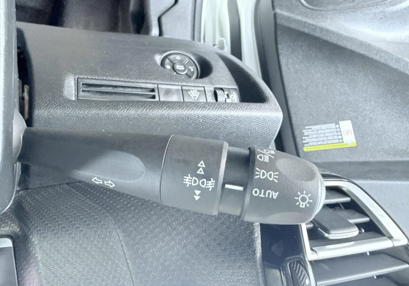 Gros plan sur la commande des phares et clignotants côté gauche du tableau de bord d'une Citroën C4 blanche 2023.