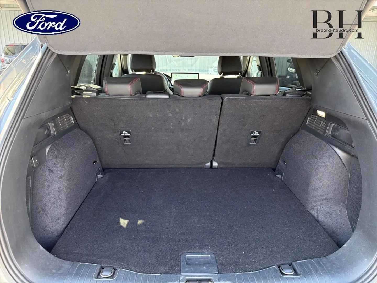 Coffre ouvert du Ford Kuga 2024 gris Solar, vue arrière montrant la banquette arrière et l'espace de chargement vide.