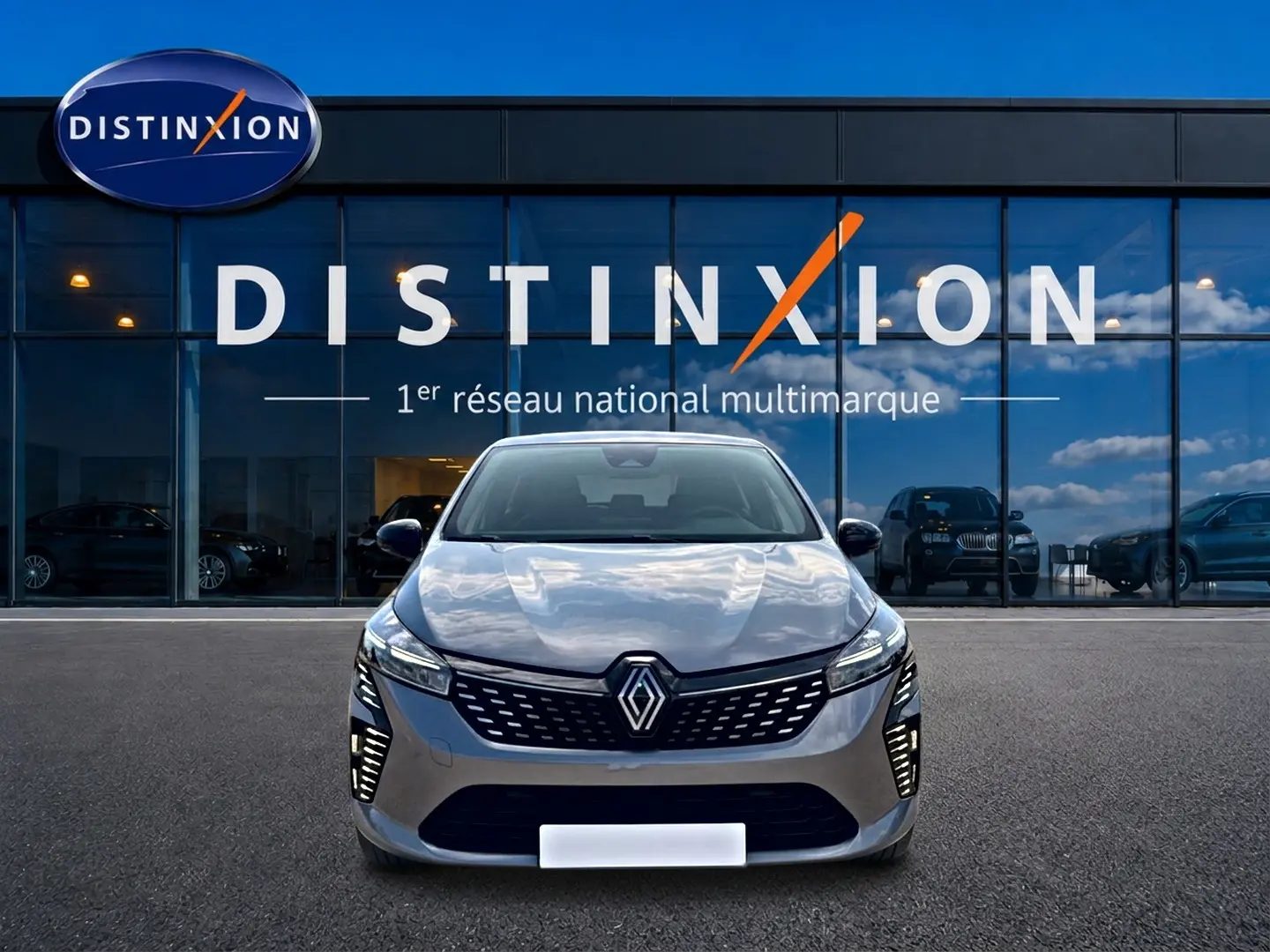 Vue frontale d'une Renault Clio V gris foncé 2025 avec calandre moderne et feux LED allumés devant un showroom Distinxion.