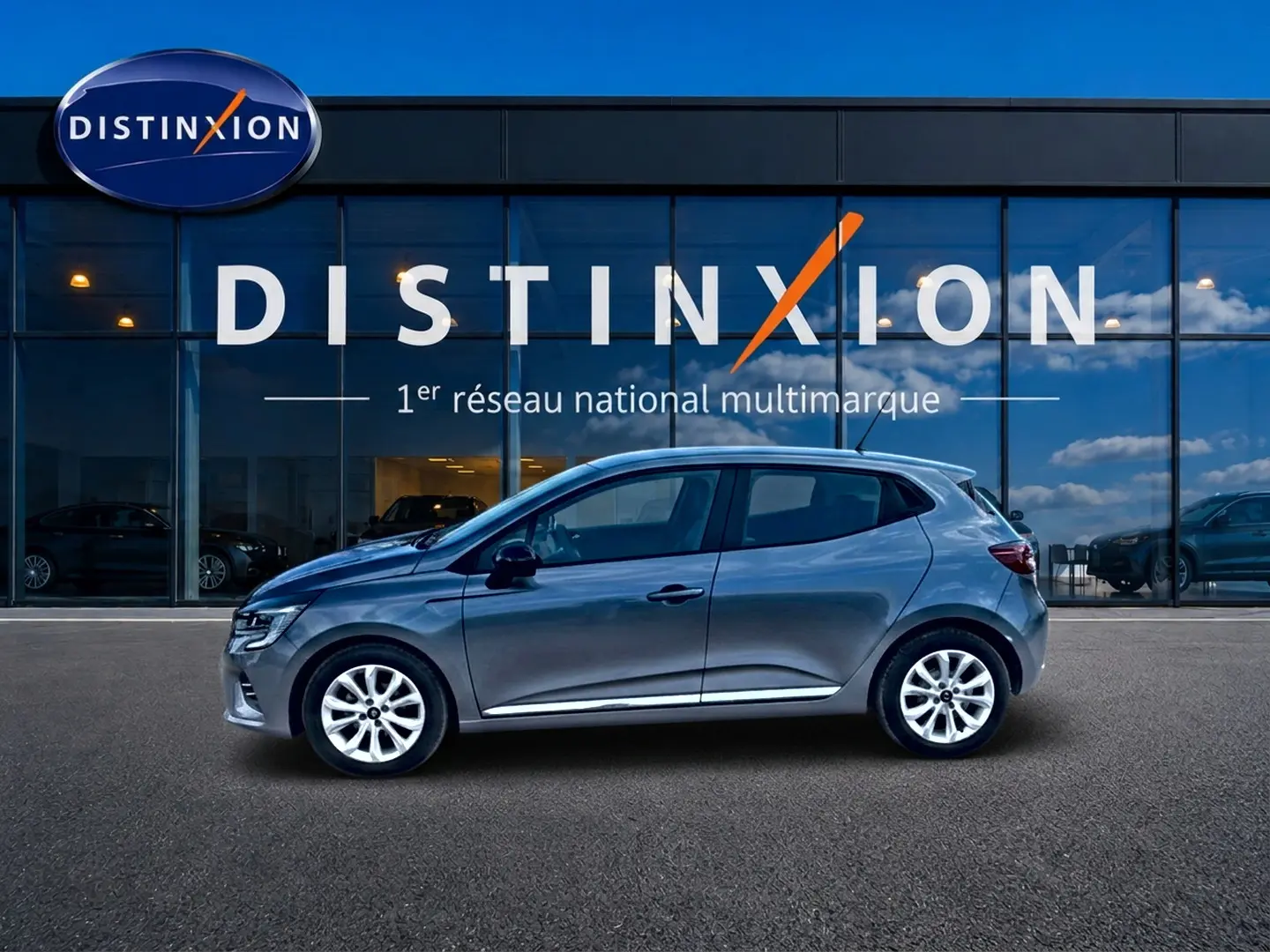 Profil droit d'une Renault Clio V gris foncé 2025 garée devant une vitrine avec logo Distinxion.