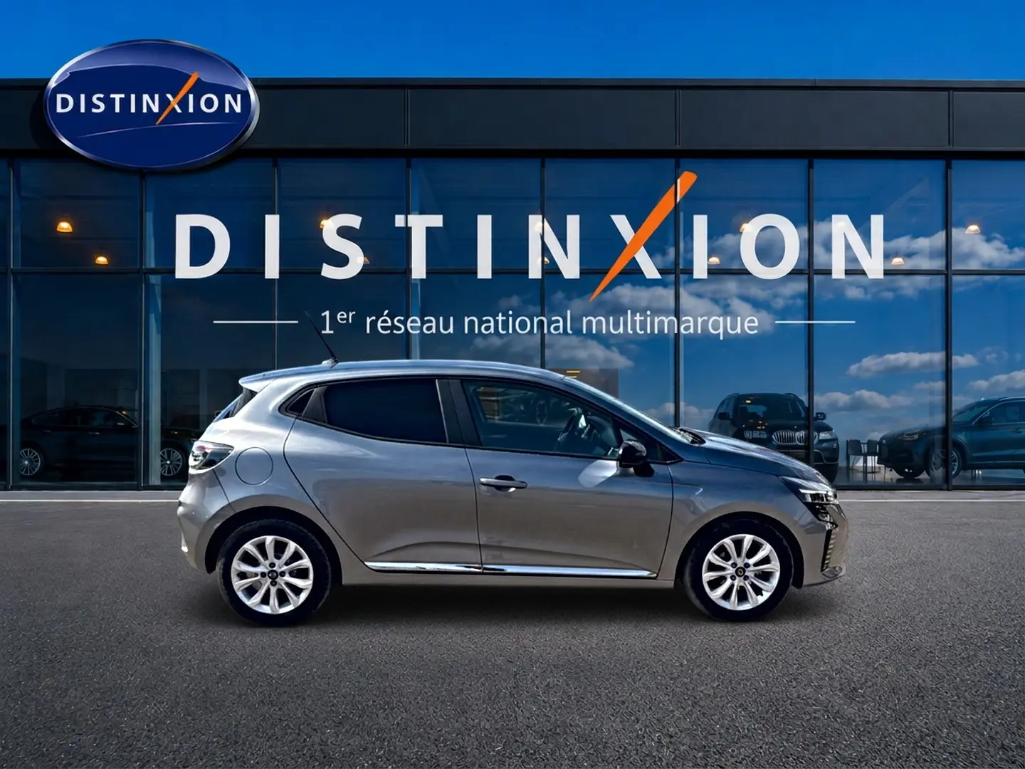 Profil droit d'une Renault Clio V gris foncé 2025, avec jantes alliage et vitres teintées, devant une vitrine Distinxion.