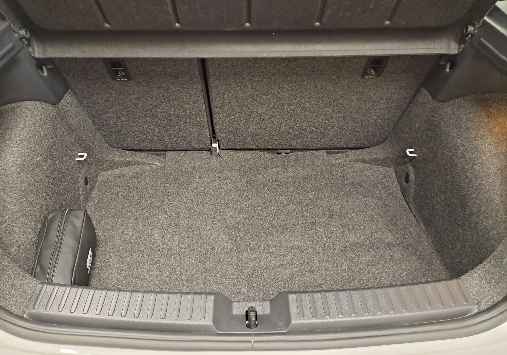 Coffre ouvert de la SEAT Ibiza blanc candy 2023, vue intérieure montrant un espace de rangement propre et un kit de secours noir.