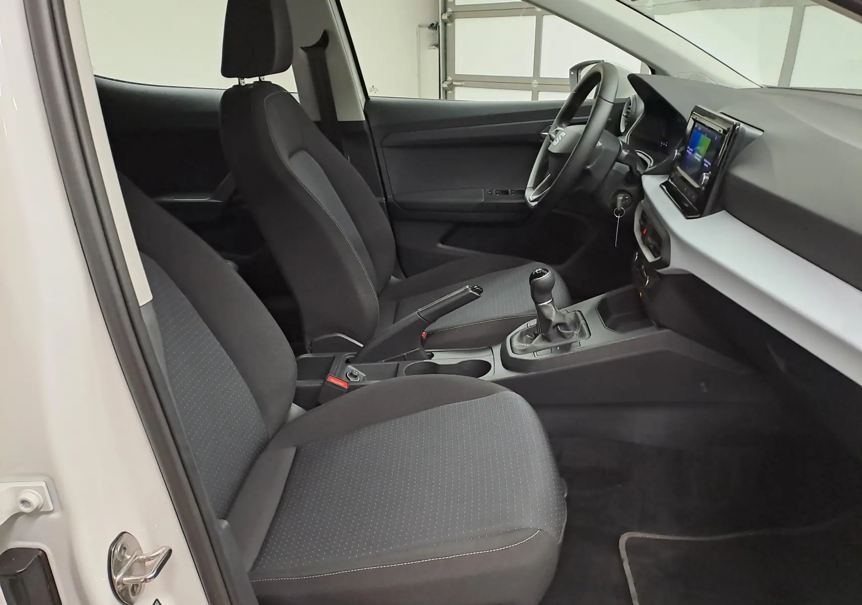 Vue intérieure côté gauche de la SEAT Ibiza 2023 blanc candy, montrant sièges noirs et tableau de bord avec écran tactile.