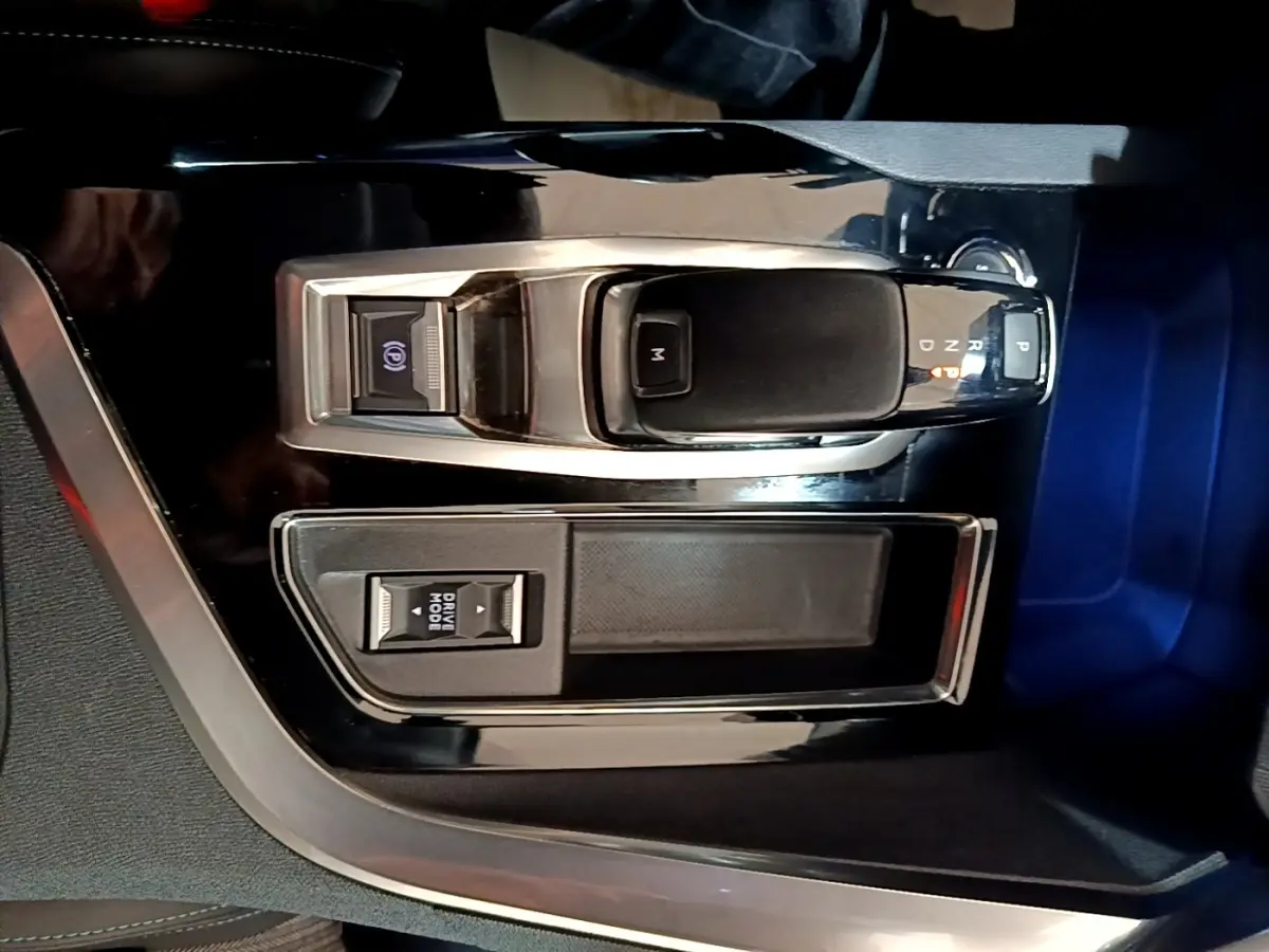 Vue rapprochée de la console centrale noire brillante avec levier de vitesse automatique et bouton mode conduite du Peugeot 3008 gris foncé.