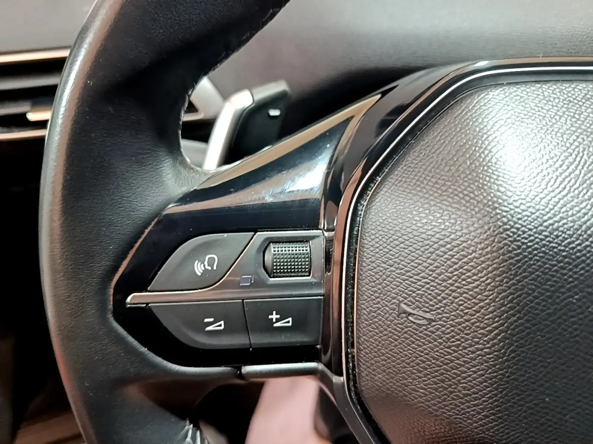 Gros plan sur le côté gauche du volant cuir noir du Peugeot 3008 gris foncé, avec commandes audio intégrées.