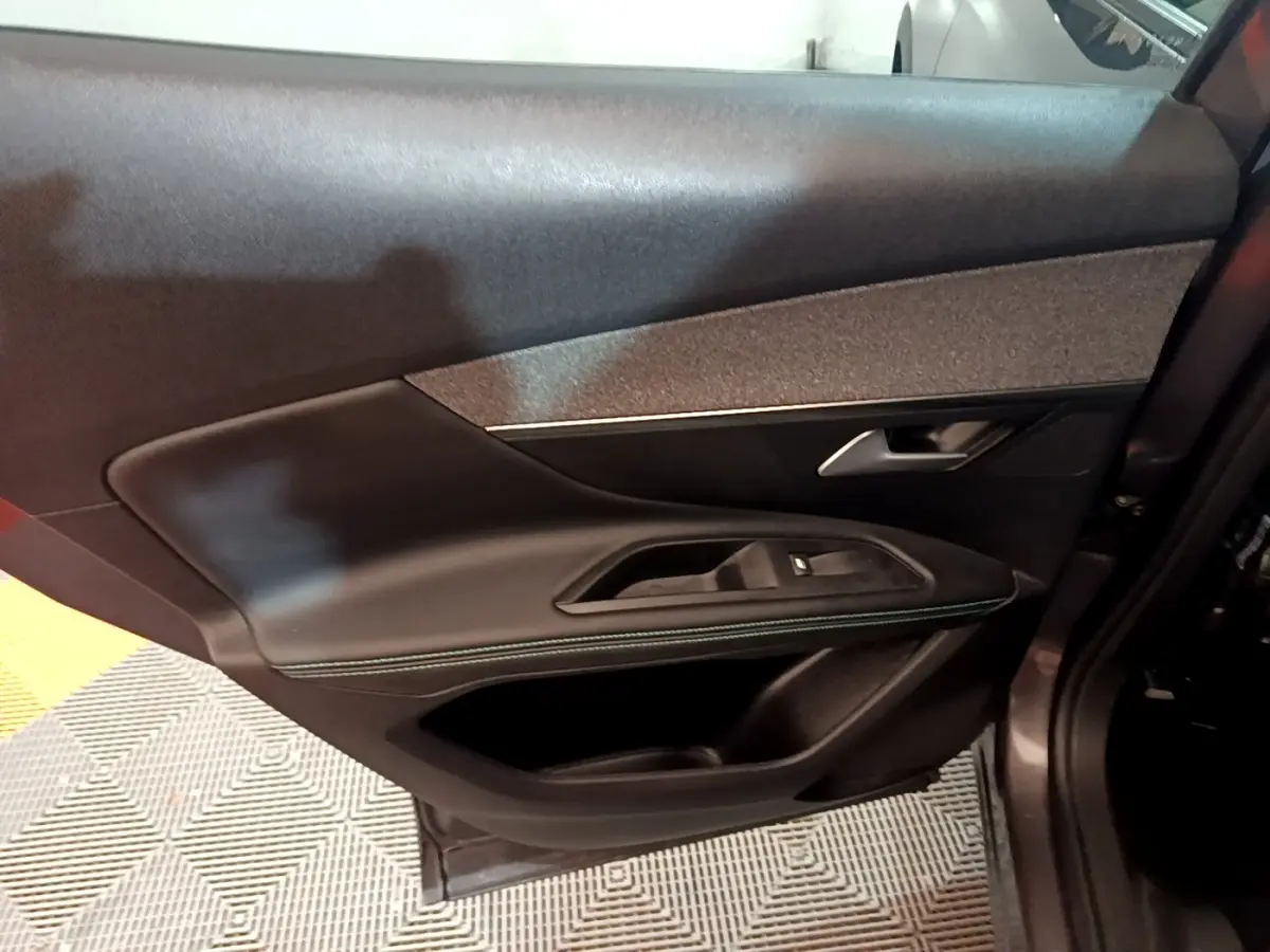 Gros plan sur la porte intérieure côté droit du Peugeot 3008 gris foncé, avec garniture cuir et surpiqûres vertes.