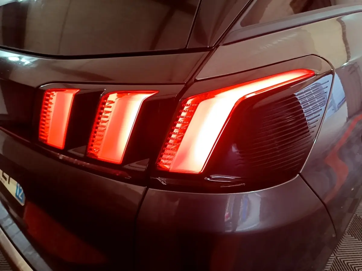 Gros plan sur le feu arrière droit allumé d’un Peugeot 3008 gris foncé, soulignant son design en trois griffes lumineuses.