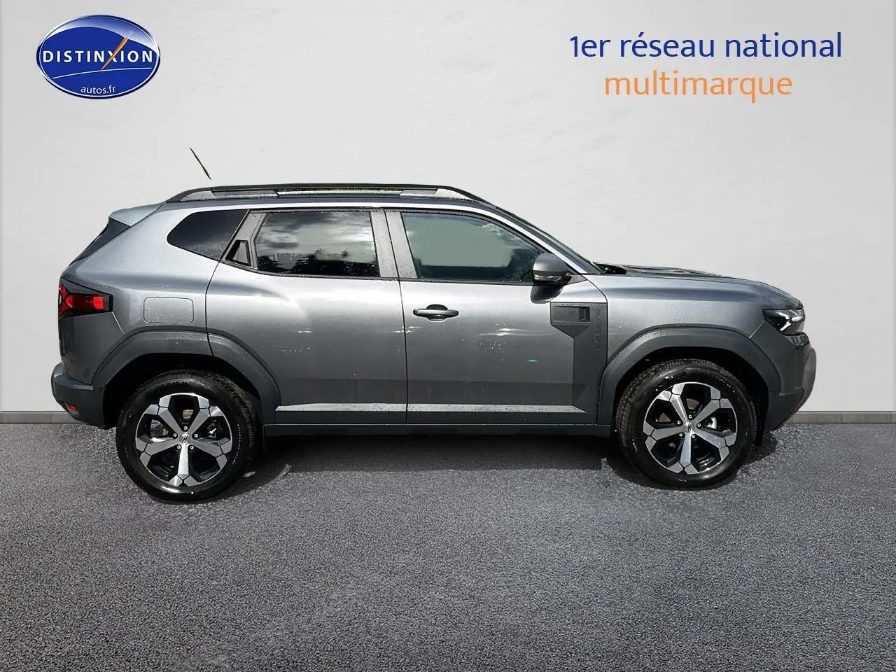 Profil droit du Dacia Duster gris schiste 2025 avec jantes alu et barres de toit visibles sur fond neutre.