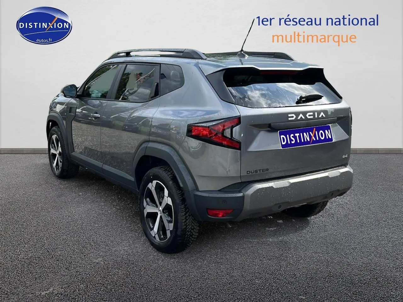 Dacia Duster gris schiste vu en 3/4 arrière droit, avec barres de toit et jantes alu distinctives.