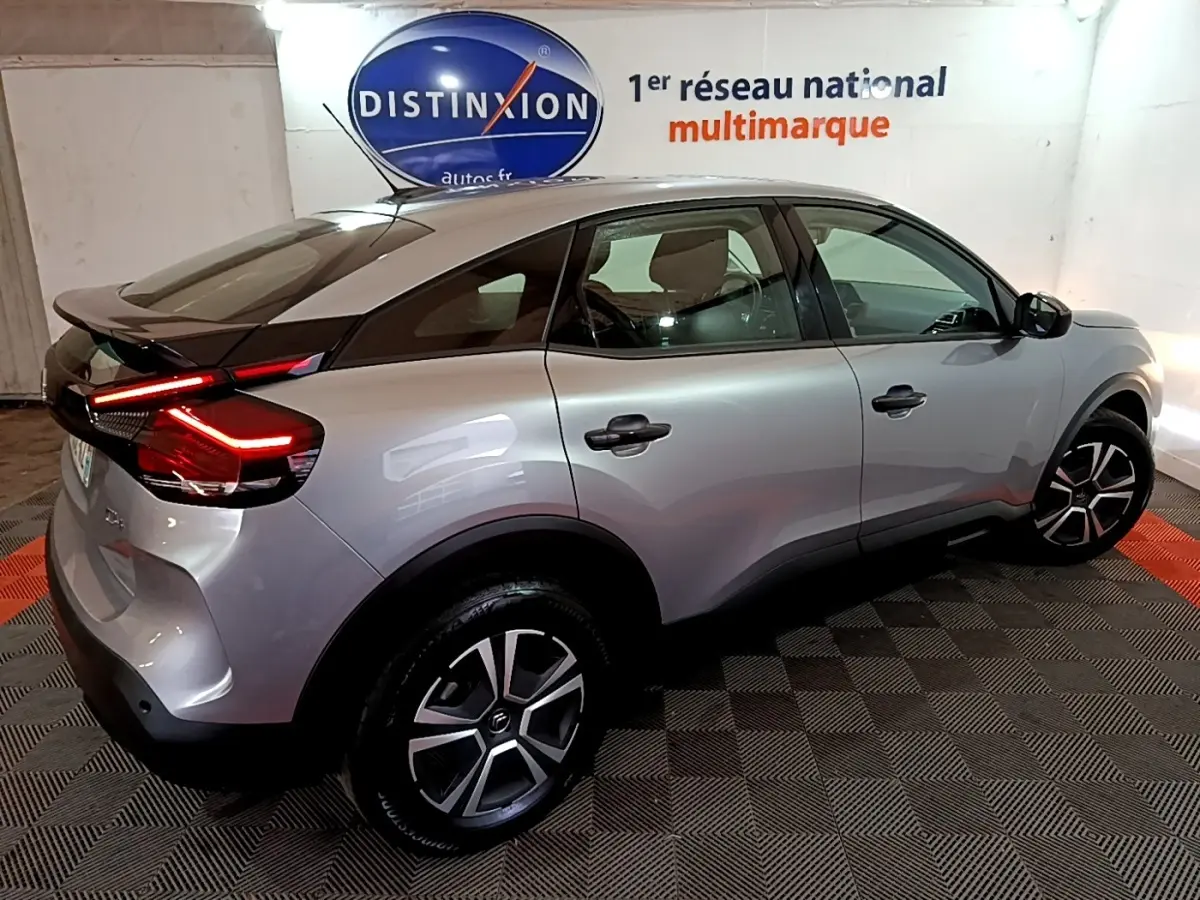 Vue 3/4 arrière droite d'une Citroën C4 gris foncé avec feux arrière LED allumés dans un showroom.