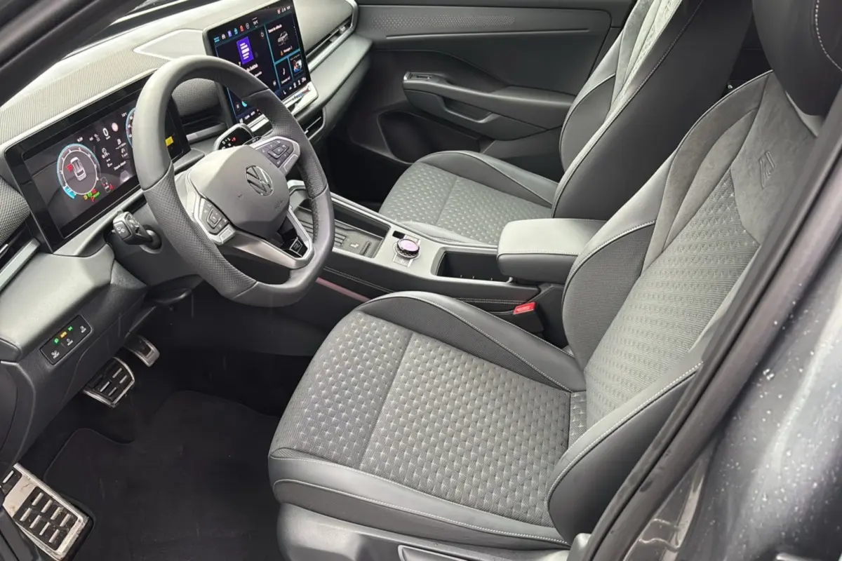 Vue intérieure côté conducteur du Volkswagen T-Roc 2026, sièges tissu gris, volant cuir multifonctions et tableau de bord digital.