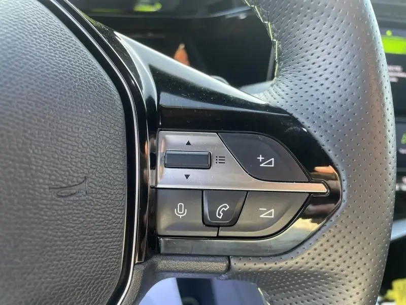 Gros plan sur les commandes au volant côté gauche du Peugeot 408 Hybrid 136 cv GT noir métal, avec boutons de volume et téléphone.
