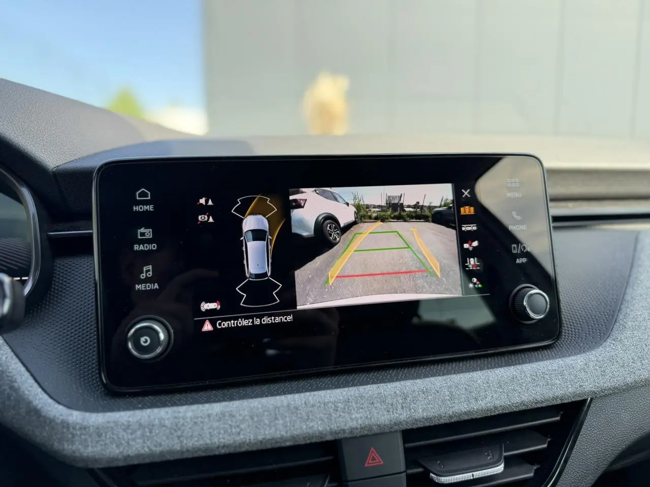 Écran central affichant la caméra de recul avec vue arrière d'une Skoda Scala blanc glacier en stationnement.