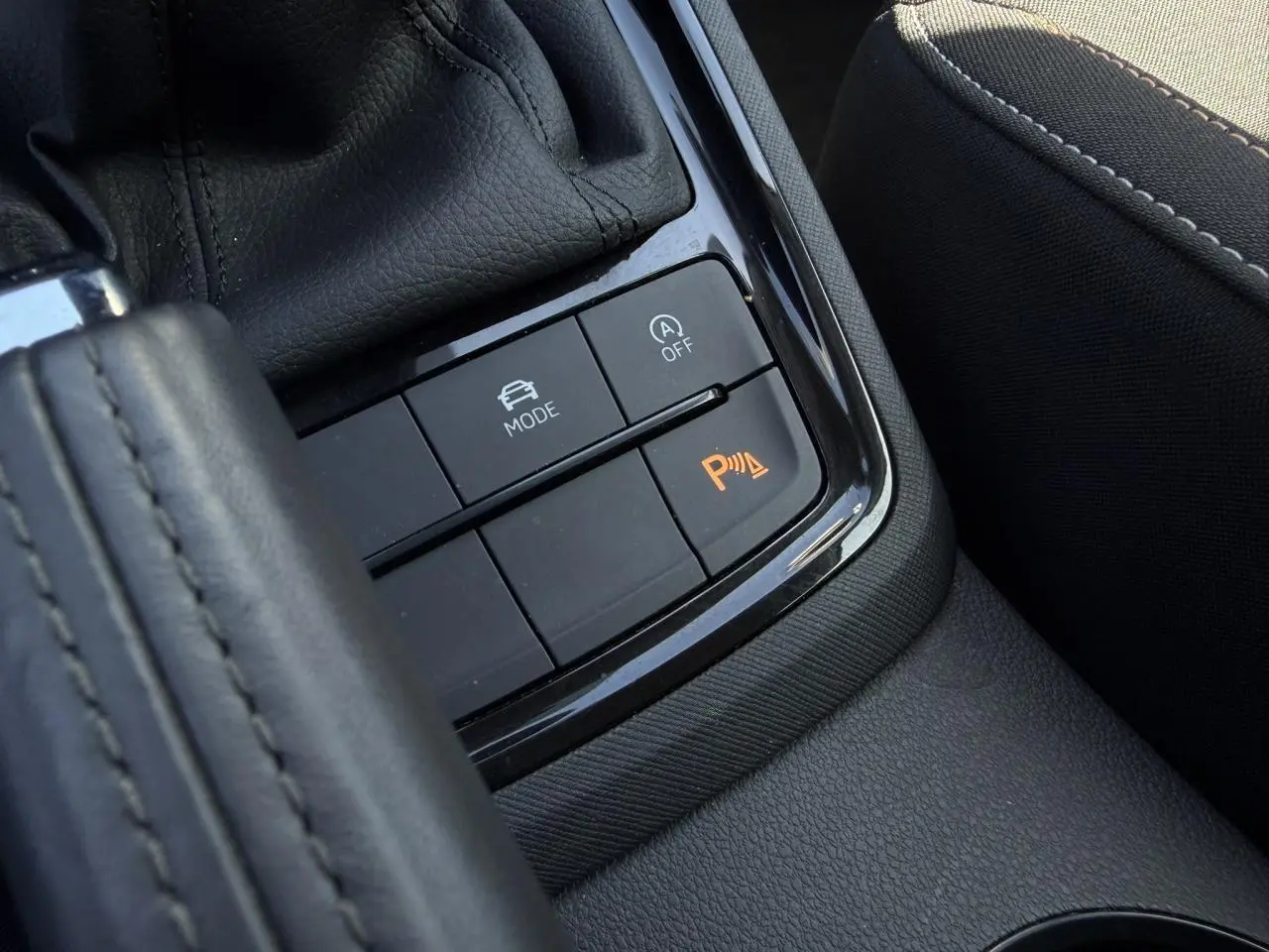 Gros plan sur la console centrale noire de la Skoda Scala TSI 116 Sélection, avec boutons de mode de conduite et aide au stationnement.