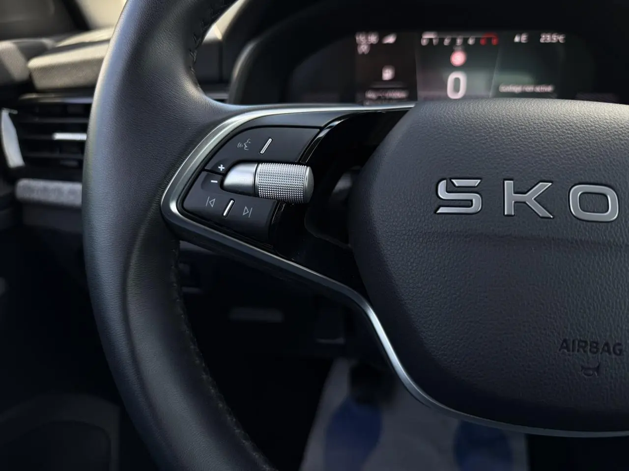 Gros plan sur le volant cuir noir de la Skoda Scala TSI 116, avec commandes multifonctions et tableau de bord digital flou en arrière-plan.