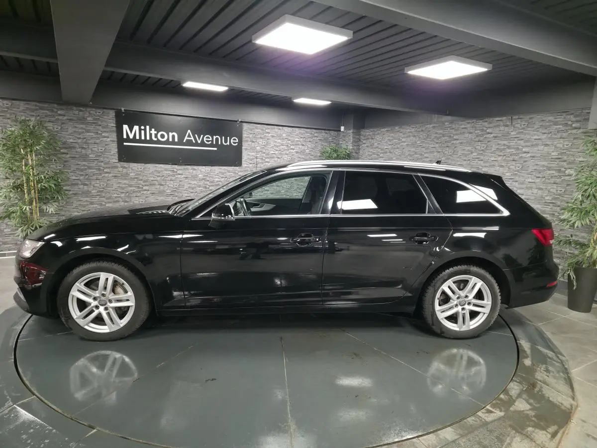 Audi A4 Avant noire vue de profil côté gauche dans un showroom avec jantes aluminium 17 pouces et rétroviseurs noir brillant.