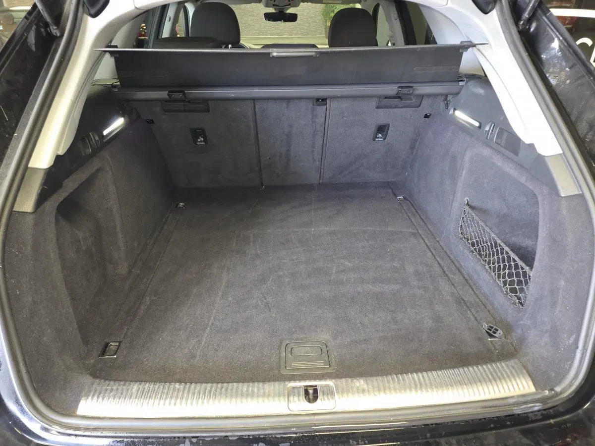 Coffre ouvert d'une Audi A4 Avant noire 2019, montrant un espace de chargement propre avec filet latéral et éclairage intégré.