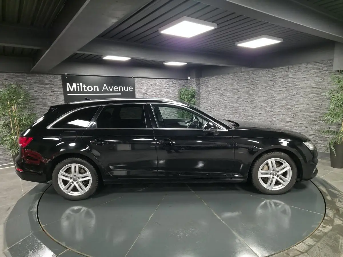 Audi A4 Avant noire vue de profil côté gauche dans un showroom avec jantes aluminium 17 pouces et rétroviseurs noirs brillants.