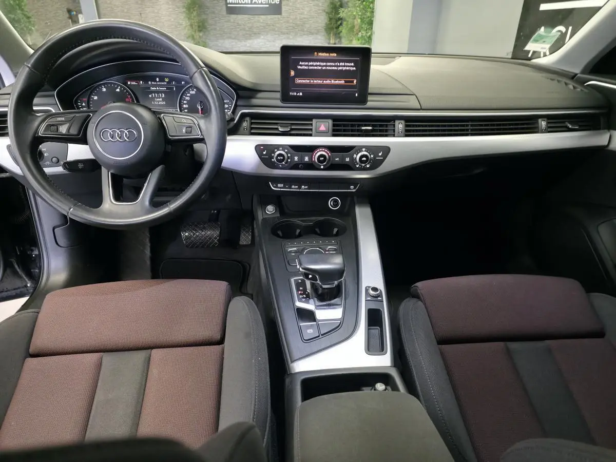 Vue intérieure avant de l'Audi A4 2019, tableau de bord avec écran central, volant cuir et console centrale avec levier de vitesses.