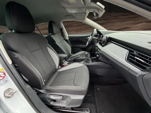 Vue intérieure côté conducteur de la Skoda Scala blanche 2025, sièges tissu noir et gris, tableau de bord moderne avec écran tactile.