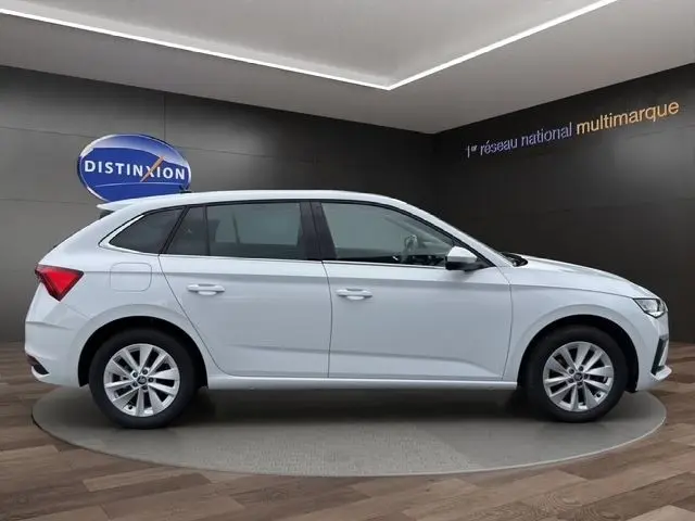 Vue de profil droit d'une Skoda Scala blanche 2025 dans un showroom avec jantes alliage et vitres teintées.