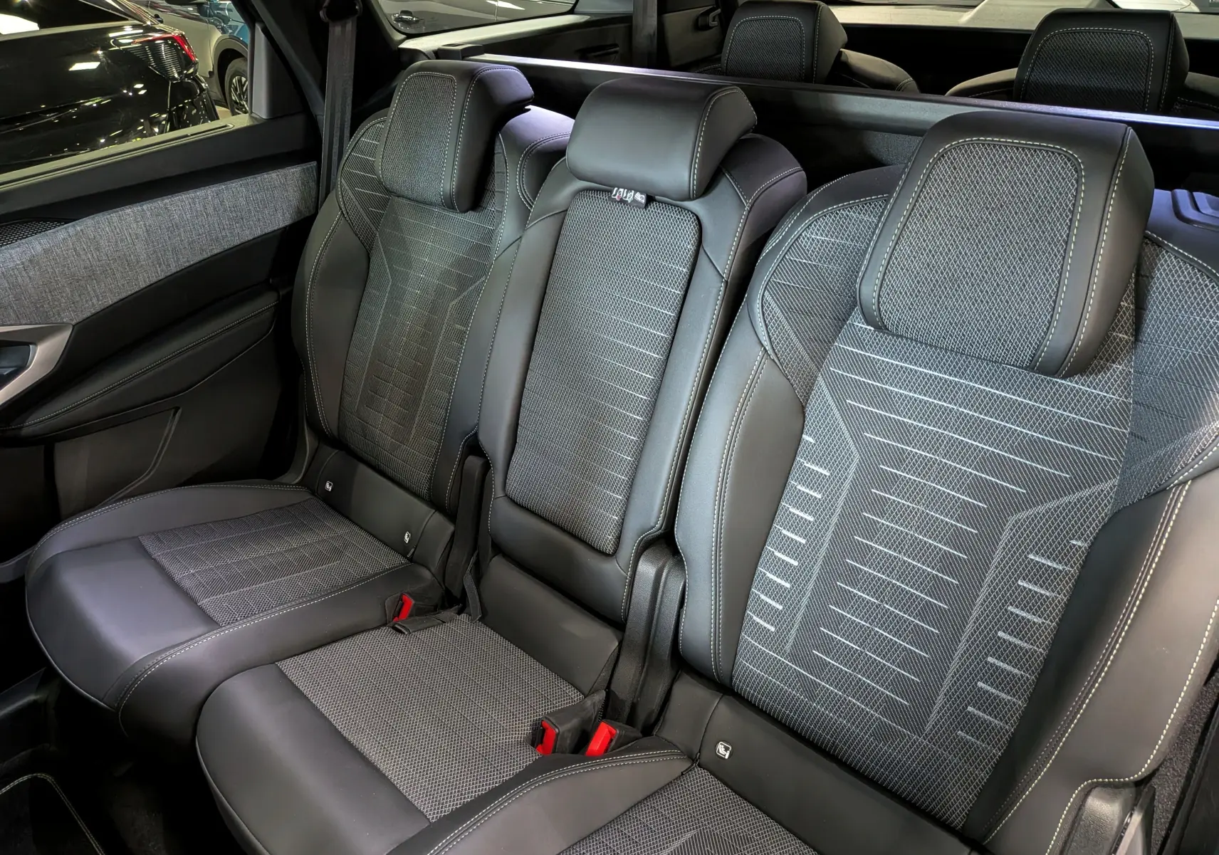 Vue intérieure sur les sièges arrière en tissu gris et cuir noir du Peugeot 5008 Hybrid 2025, avec appuie-têtes intégrés.