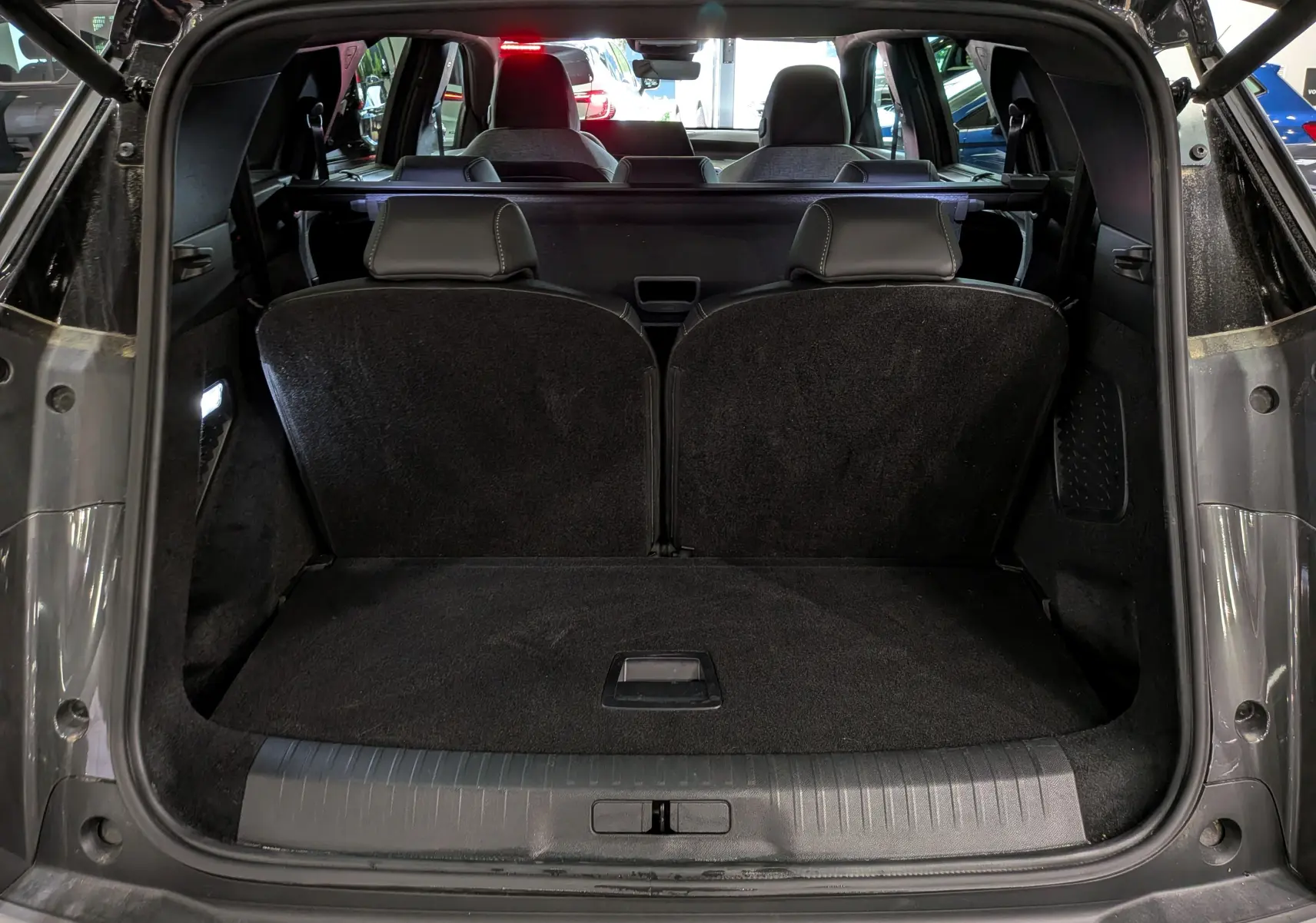 Coffre ouvert vu de l'arrière d'un Peugeot 5008 gris titane avec intérieur noir et sièges rabattus partiellement.