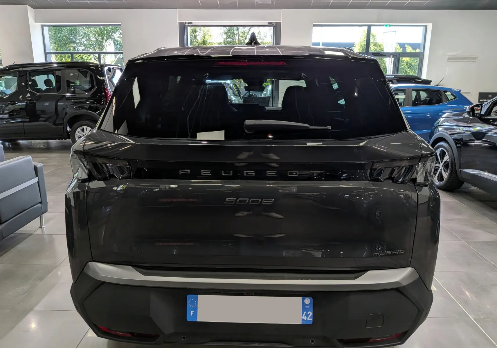 Vue arrière d’un Peugeot 5008 Hybrid gris titane avec toit noir, en showroom, soulignant son design moderne et épuré.