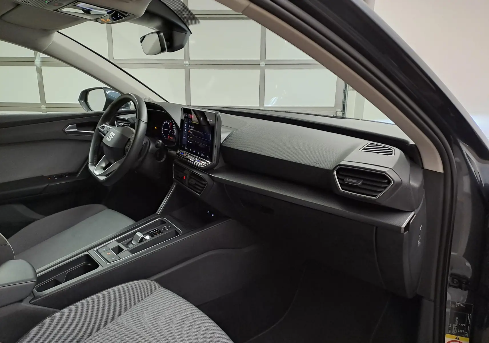 Vue intérieure côté conducteur du SEAT LEON 1.5 eTSI Hybrid 2025, tableau de bord moderne avec écran tactile central.