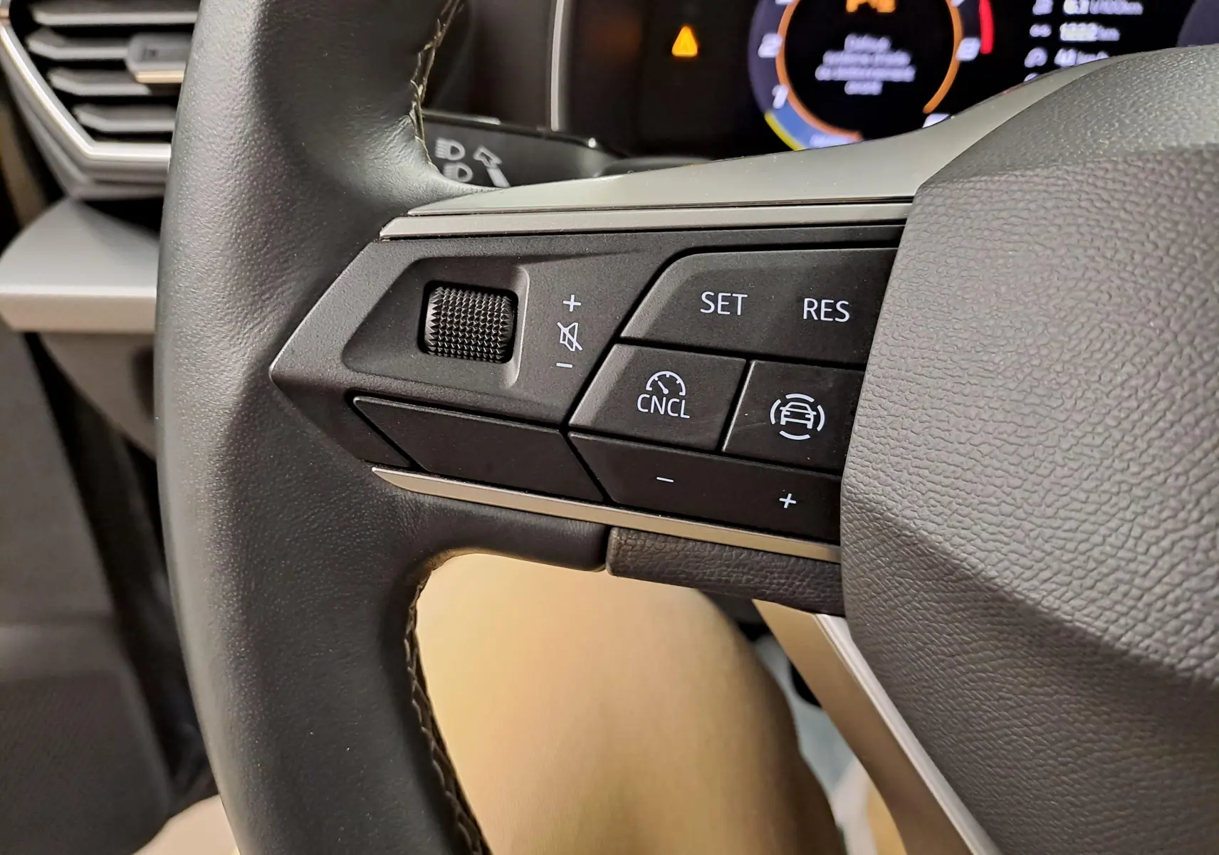 Gros plan sur les commandes au volant à gauche du SEAT LEON 1.5 eTSI Hybrid gris magnétique, avec affichage numérique en arrière-plan.