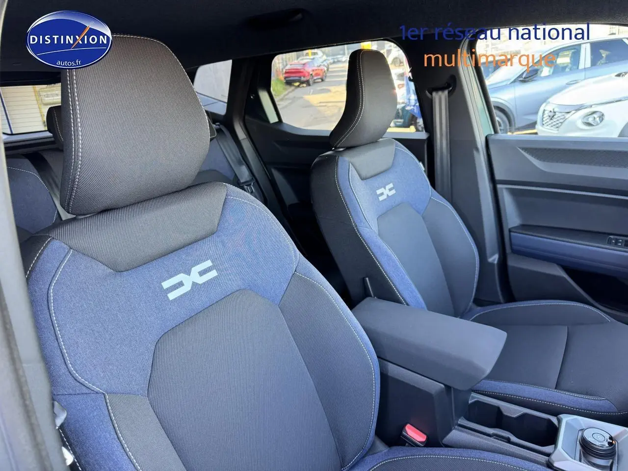Vue intérieure des sièges avant bleu et noir du Dacia Duster 2025 avec accoudoir central et logo distinctif brodé.