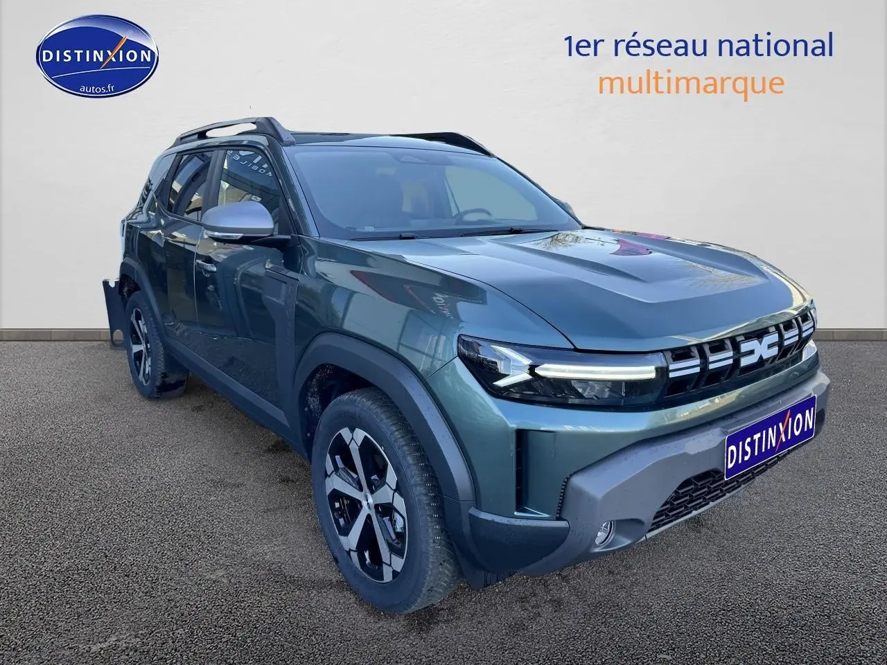 Vue 3/4 avant gauche d'un Dacia Duster 2025 vert cèdre avec jantes alu et barres de toit visibles.