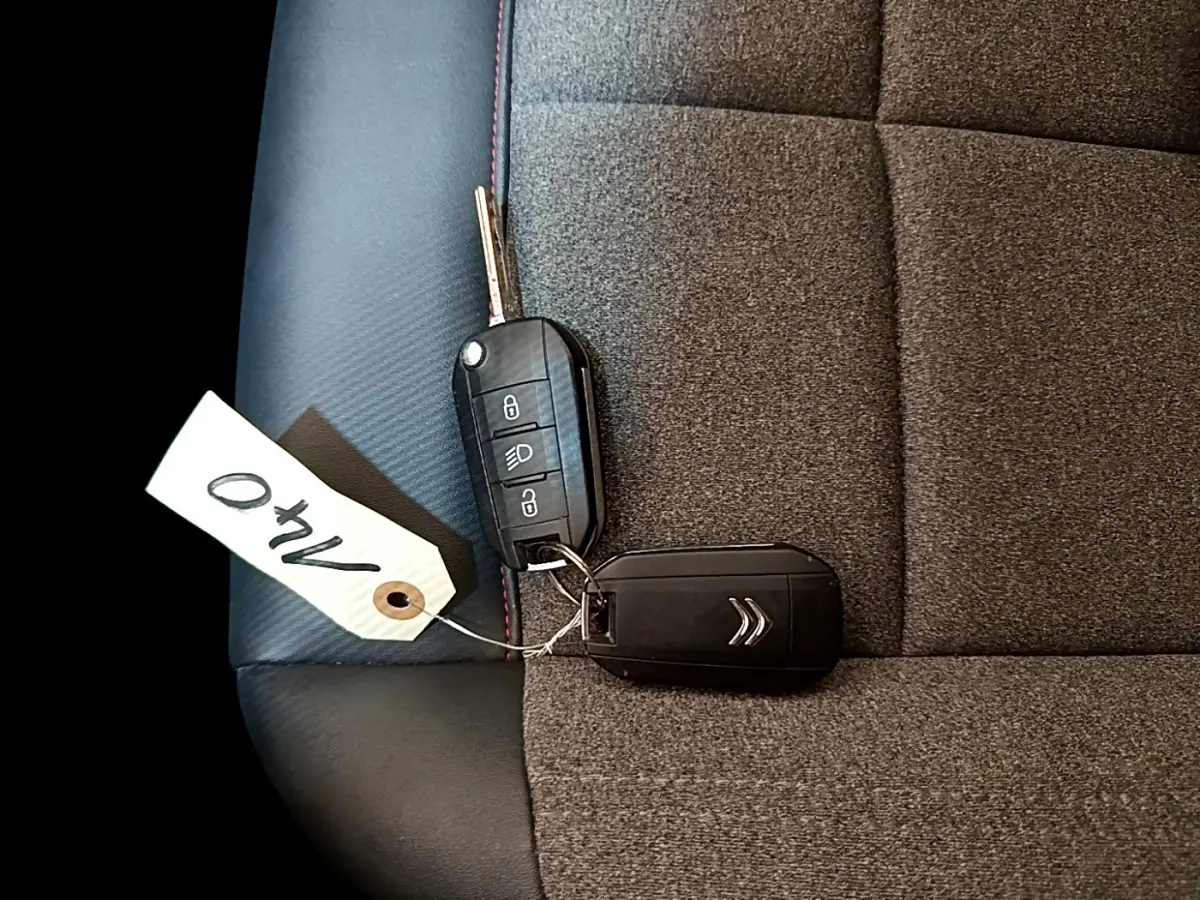 Gros plan sur la clé noire Citroën posée sur un siège tissu gris foncé avec surpiqûres rouges.