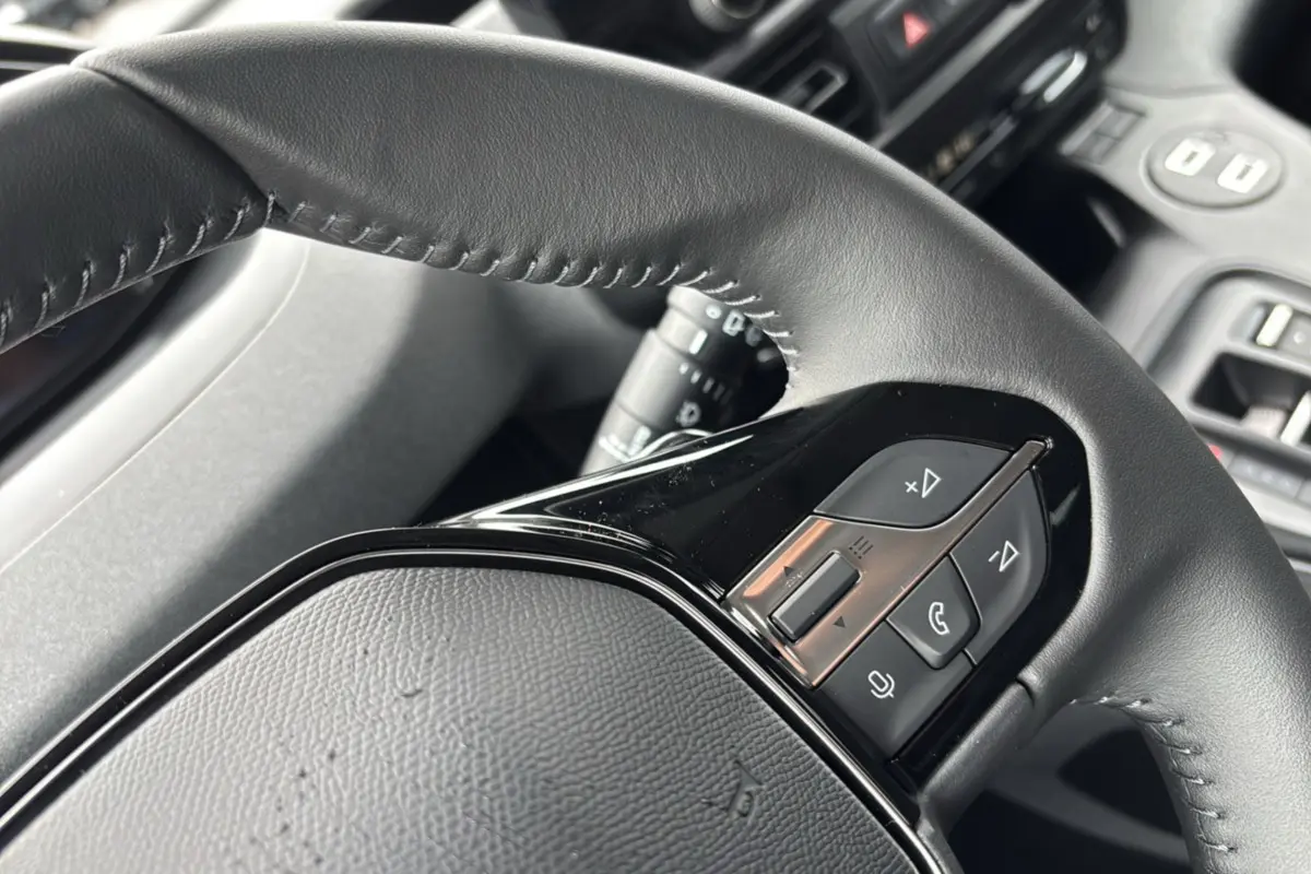 Gros plan sur le volant cuir noir du Peugeot Rifter 2026 avec commandes multifonctions et surpiqûres visibles.