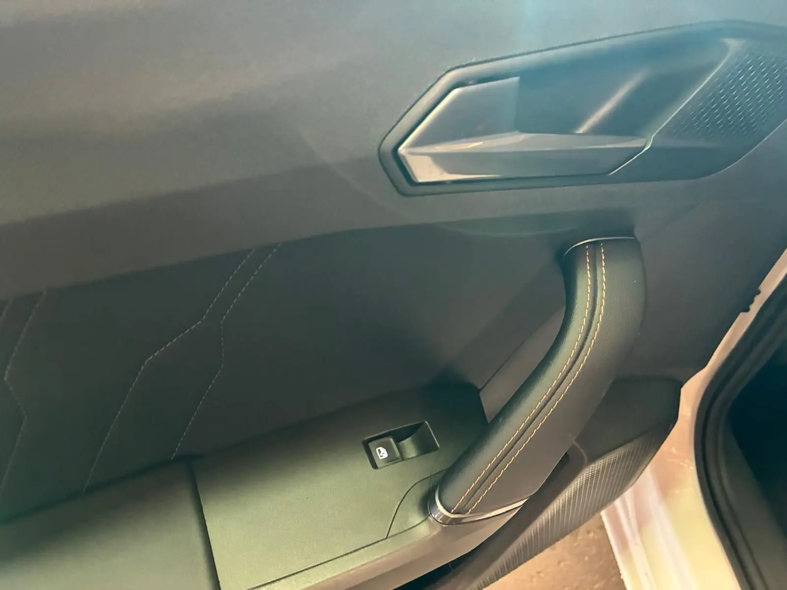 Poignée de porte intérieure côté gauche avec couture orange sur fond noir, partie d’une CUPRA LEON ST blanche 2024.