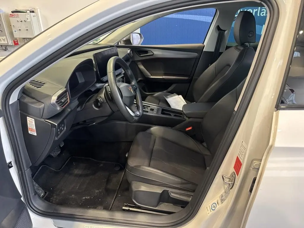Vue intérieure côté conducteur d'une CUPRA LEON ST blanche 2024 avec sièges noirs en cuir et tableau de bord moderne.