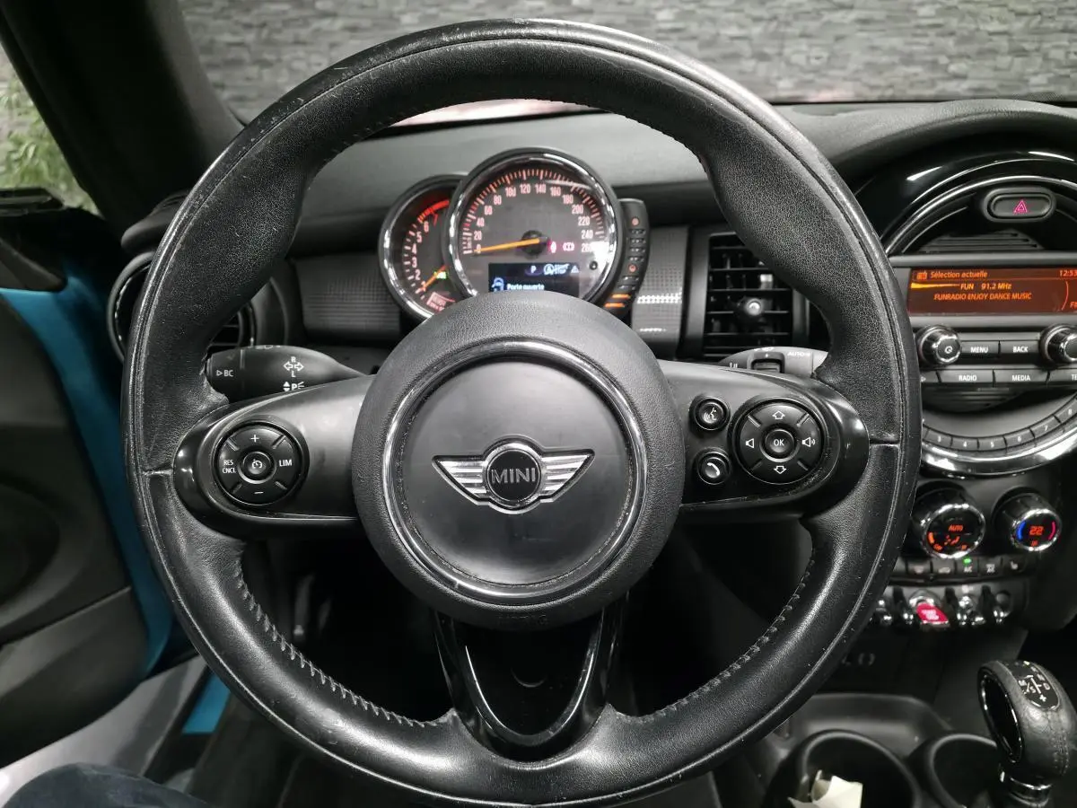 Vue centrée sur le volant en cuir noir d'une MINI Cabriolet bleu, avec tableau de bord et console centrale visibles.