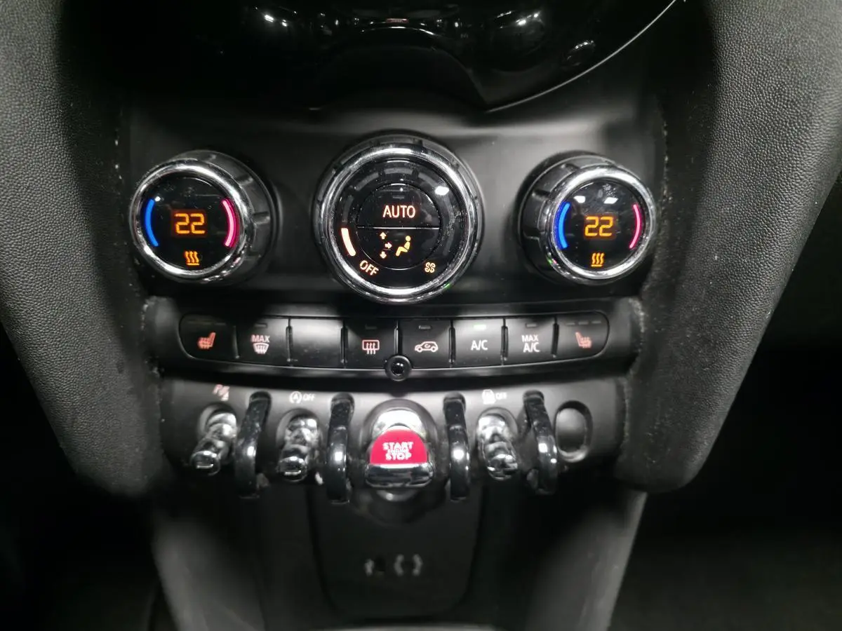 Gros plan sur la console centrale du MINI Cabriolet bleu, affichant la climatisation automatique et le bouton Start/Stop rouge.