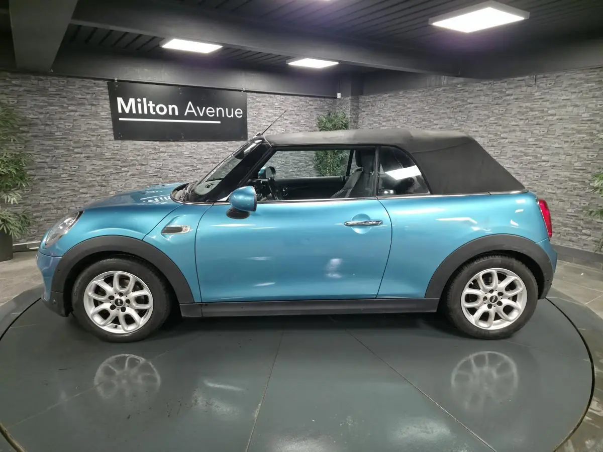 Vue de profil côté gauche d'une MINI Cabriolet bleu avec capote noire et jantes argentées en intérieur showroom.
